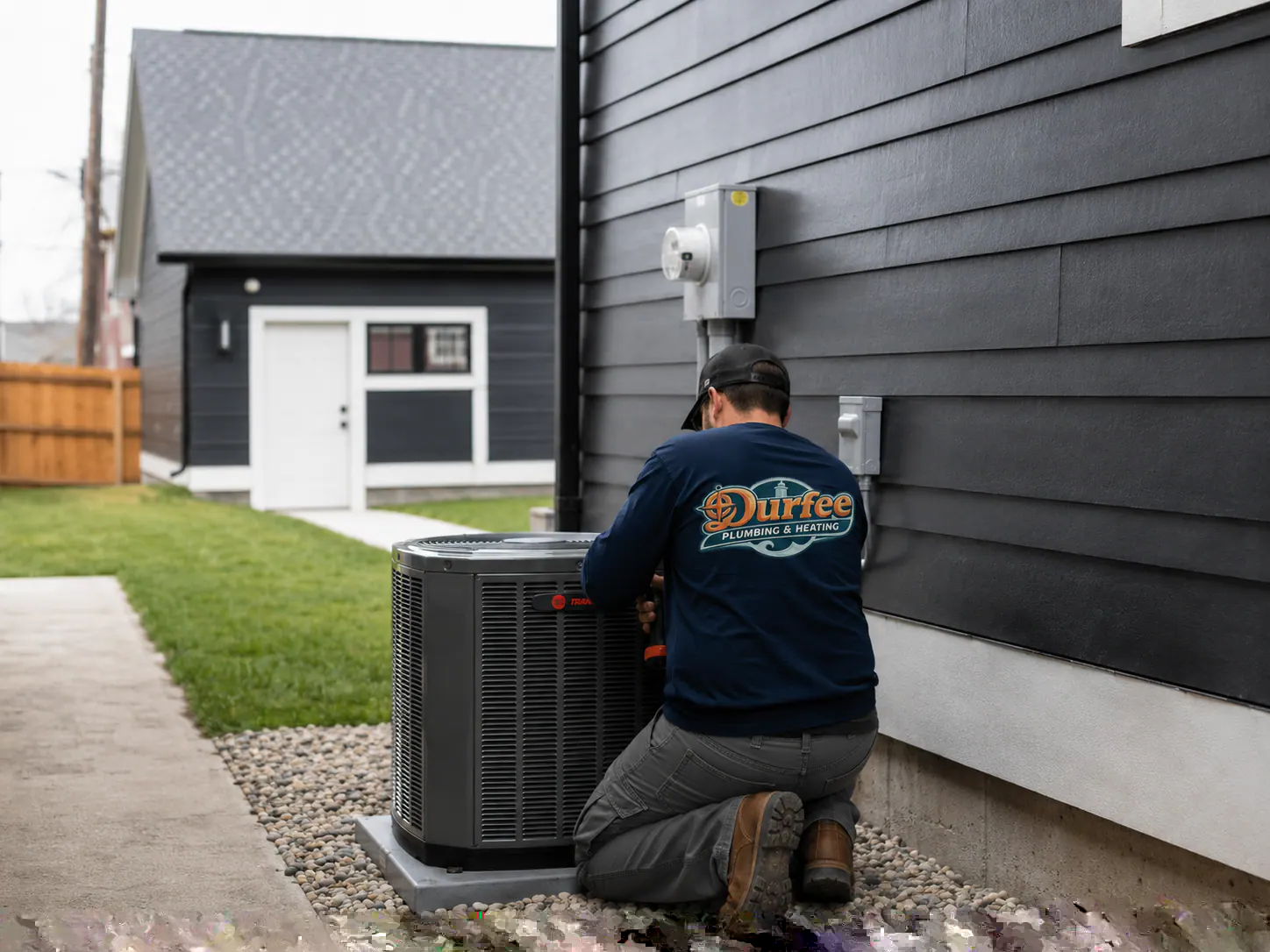 A technician servicing an outdoor AC condenser beside a home.